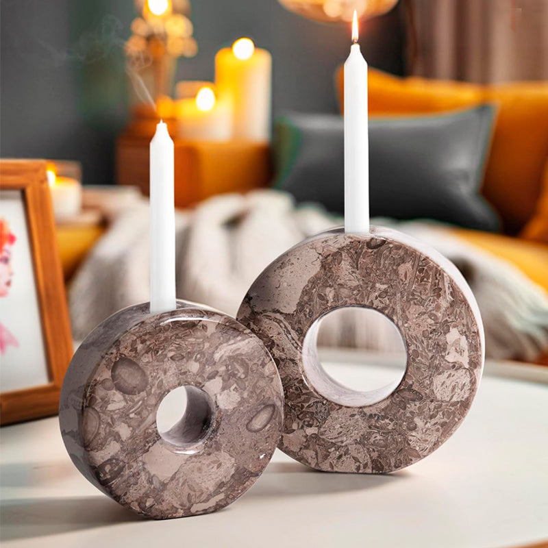Two stone-like candle holders with candles on a table in a cozy indoor setting.