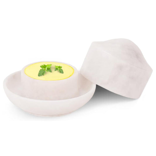 White ceramic egg holder with a cracked open egg containing a yellow yolk and green herbs on a white background