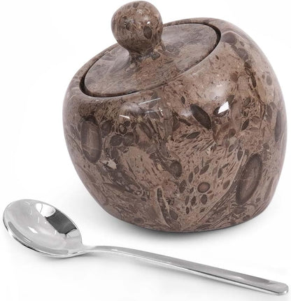 Decorative ceramic sugar bowl with a lid and a silver spoon on a white background