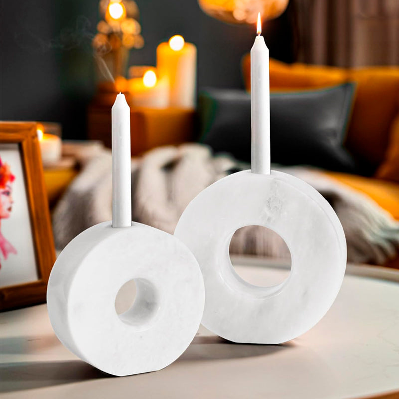 Two white marble candle holders with candles on a table in a cozy indoor setting.
