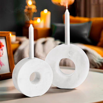 Two white marble candle holders with candles on a table in a cozy indoor setting.