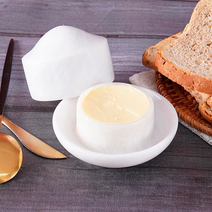 White ceramic butter dish with a lid on a wooden table with bread and a knife.