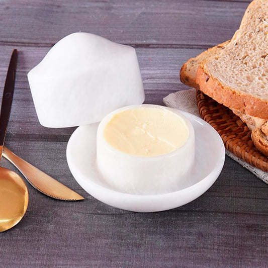 White ceramic butter dish with a lid on a wooden table with bread and a knife.