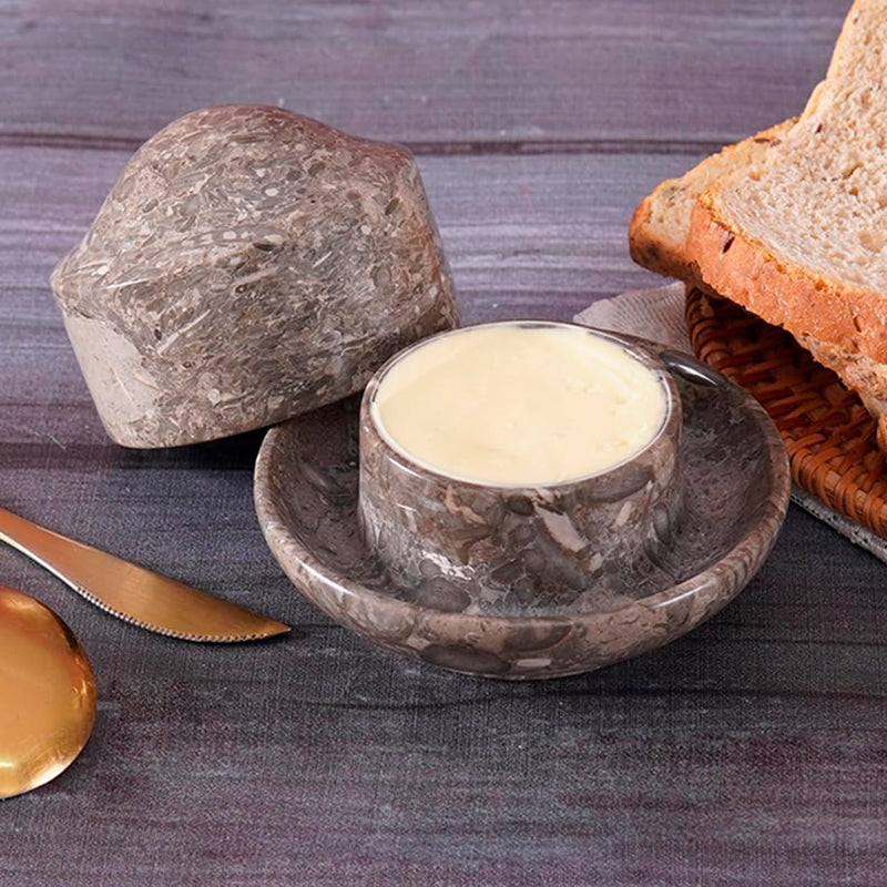 Butter dish with a stone lid on a wooden surface with bread and a knife.