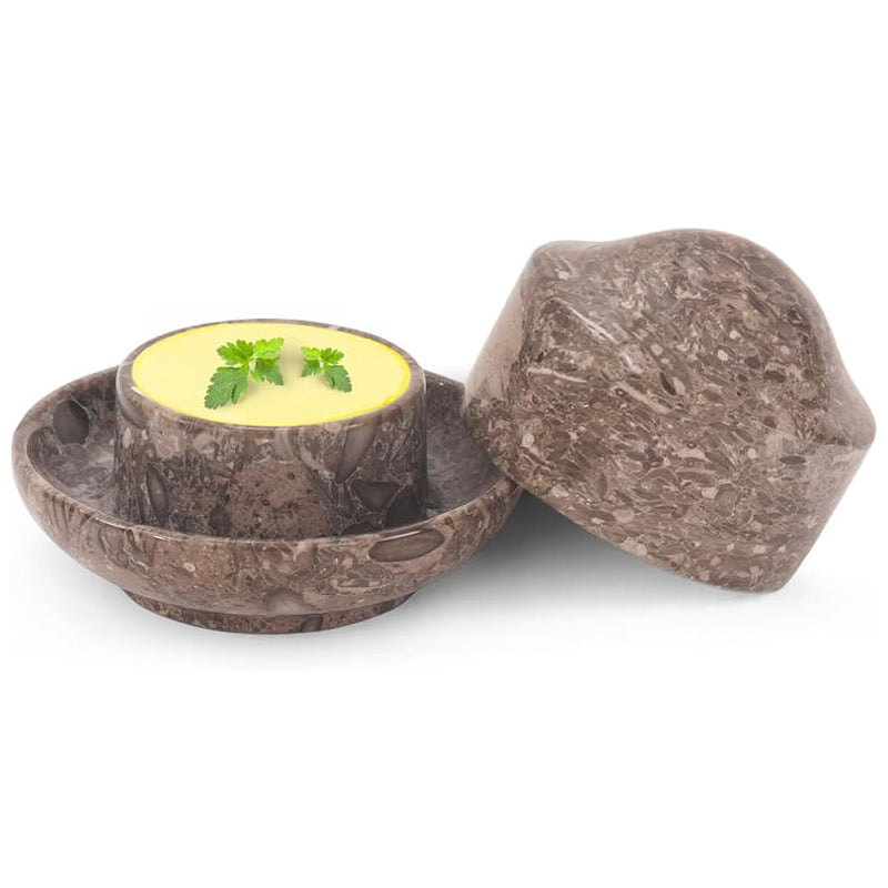Brown stone-like container with a lid, holding a yellow substance and green leaves on a white background