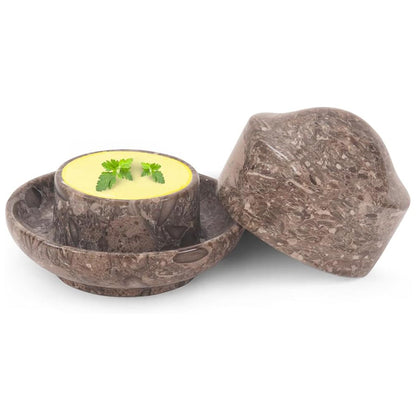 Brown stone-like container with a lid, holding a yellow substance and green leaves on a white background