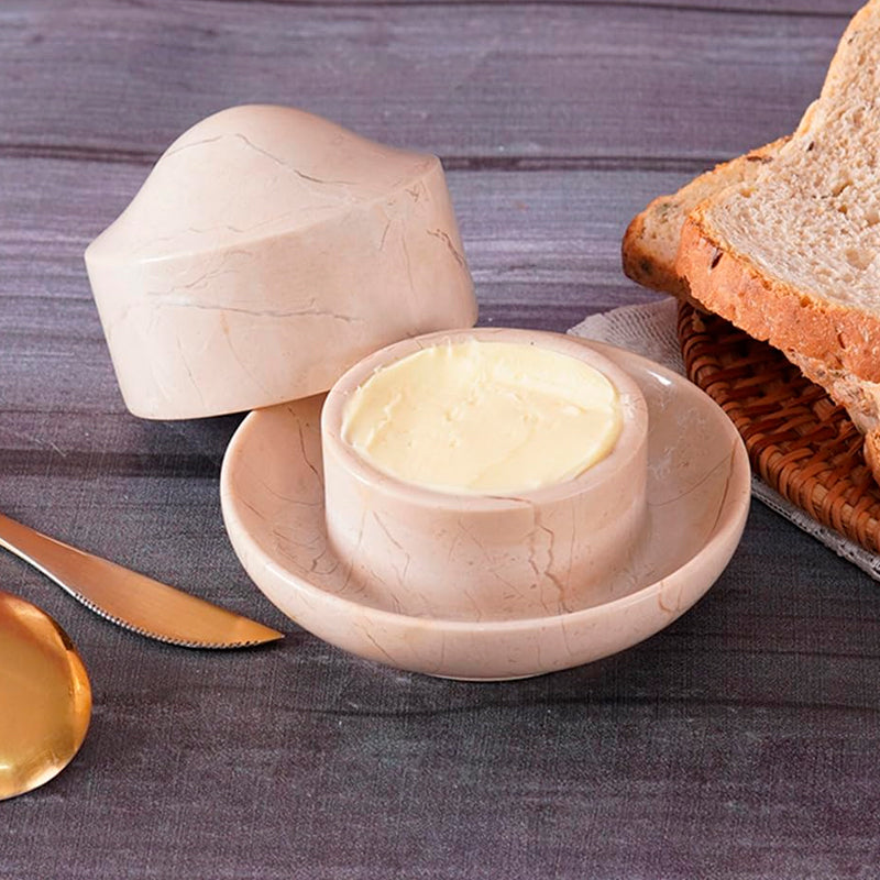 Butter dish with marble texture containing butter, next to bread and a knife on a wooden surface.