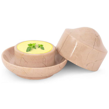Wooden bowl with a cracked design containing a yellow substance and green leaves, on a white background.