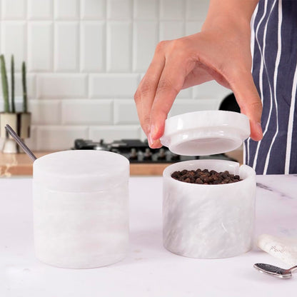 Person opening a white marble container filled with coffee beans on a kitchen counter.